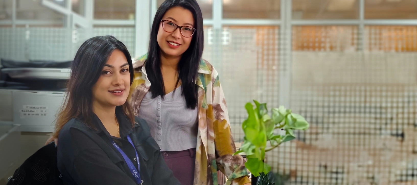 Two colleagues in an office cubicle, smiling towards the camera