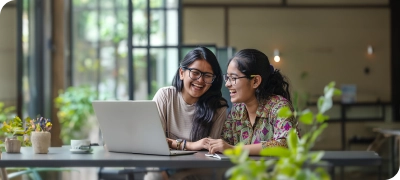 Two women sitting at a table looking at a laptop.