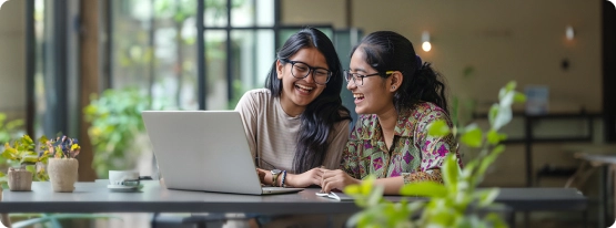 Two women sitting at a table looking at a laptop.